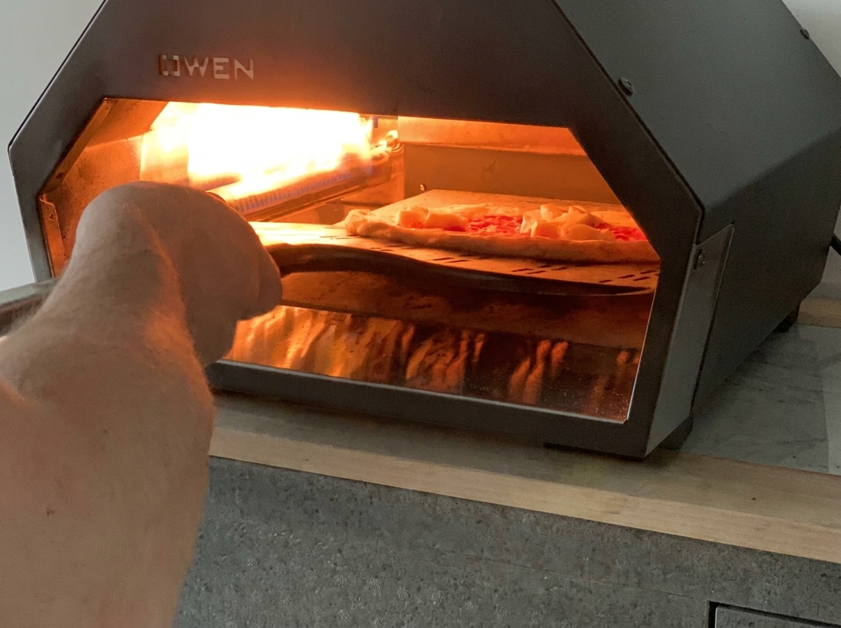 Eine ungebackene Margherita-Pizza wird mit einem Schieber in einen heißen Gas-Tischpizzaofen befördert.