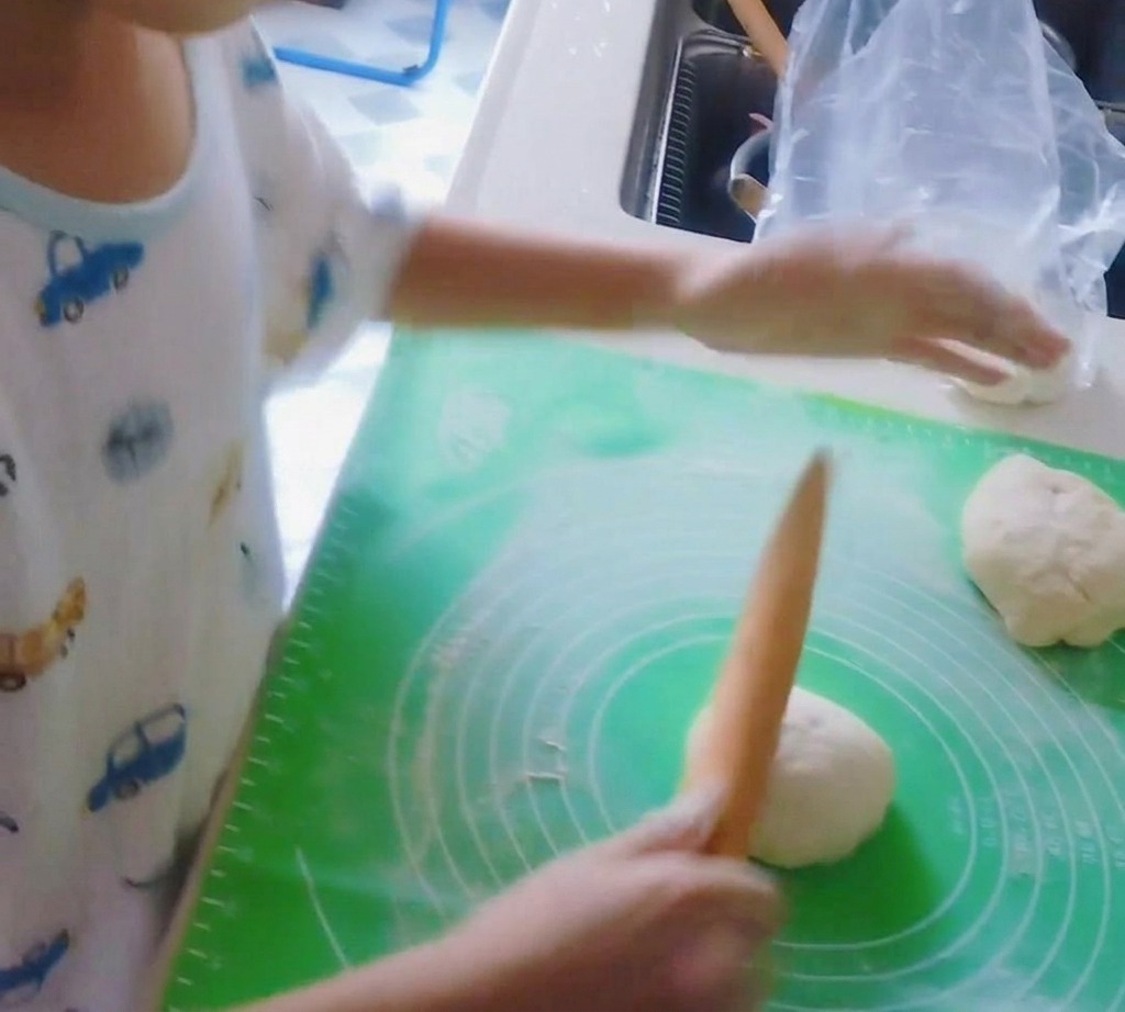 Ein hölzernes Nudelholz rollt eine Pizzateigkugel flach.