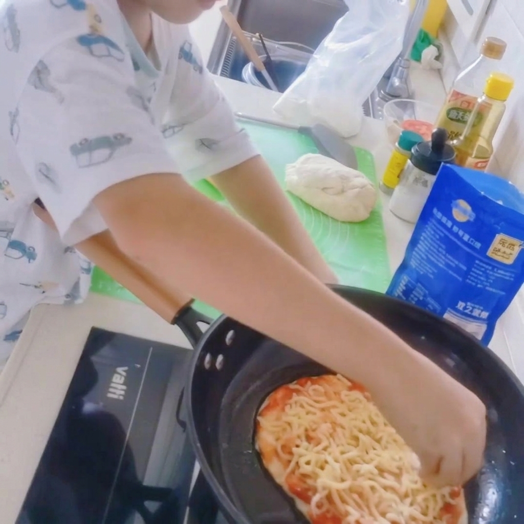 Nahaufnahme einer Pizza in einer Pfanne, die mit einer Schicht Mozzarella belegt wird.