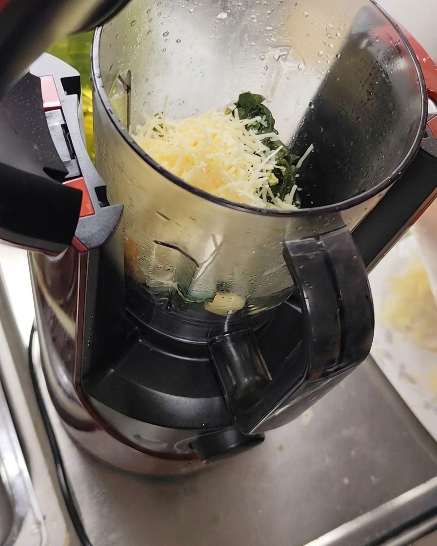 Zutaten wie geriebener Käse, Knoblauch und Pinienkerne werden zusammen mit Basilikum in einen Zerkleinerer gegeben.