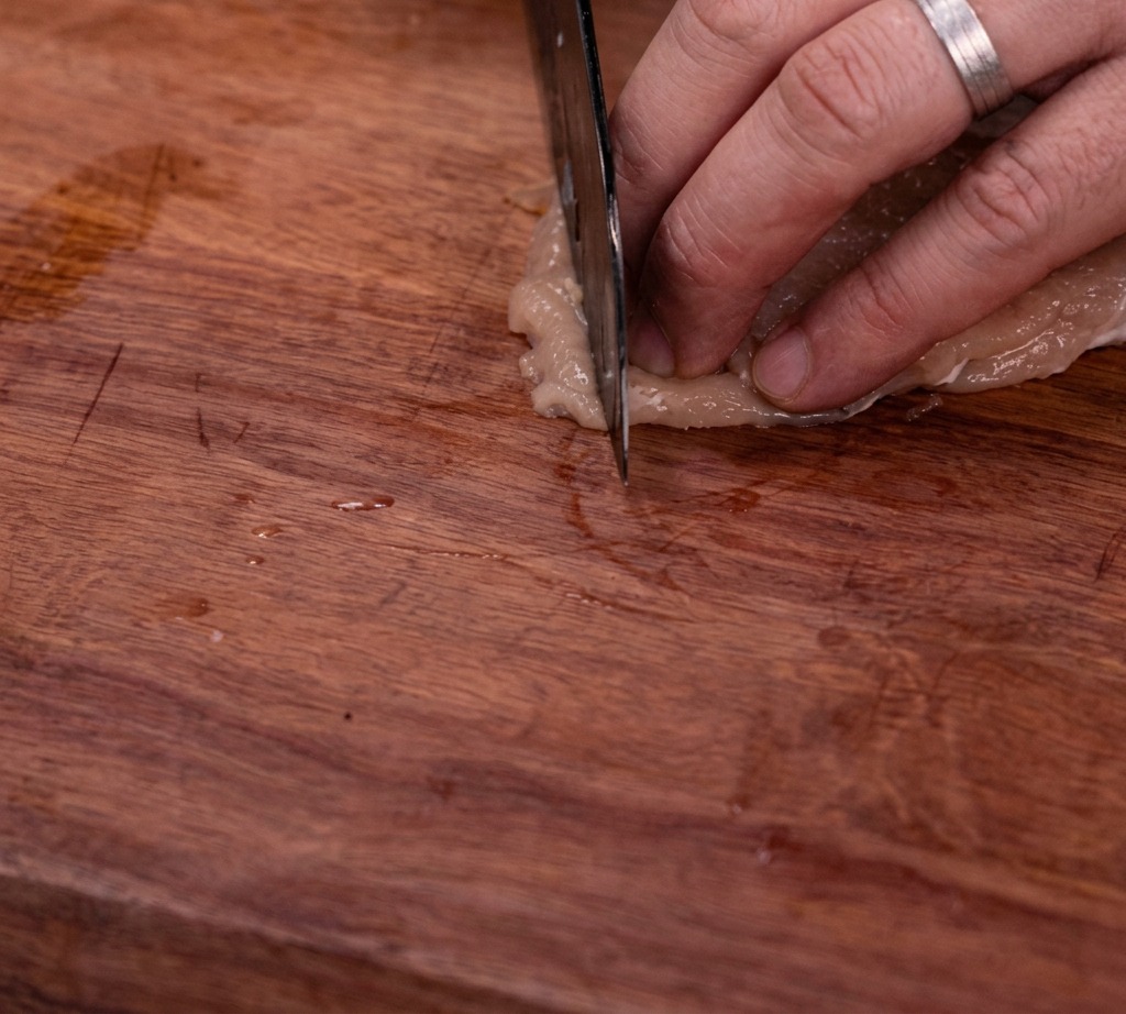 Rohe Hähnchenbrust wird auf einem Holzbrett in gleichmäßige Streifen geschnitten.