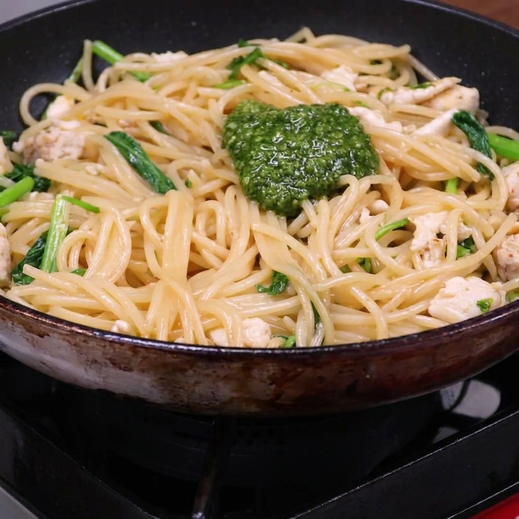 Ein Klecks Pesto auf der Pasta-Hähnchen-Mischung in der Pfanne.
