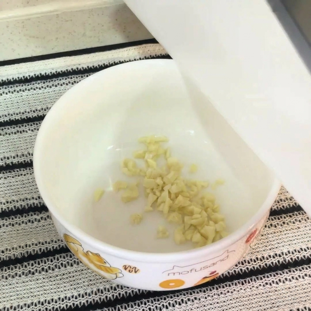 Nahaufnahme einer weißen Schüssel mit gehacktem Knoblauch, rohem Eigelb, Instant-Nudel-Gewürz und Mayonnaise, bereit zur Vermischung.