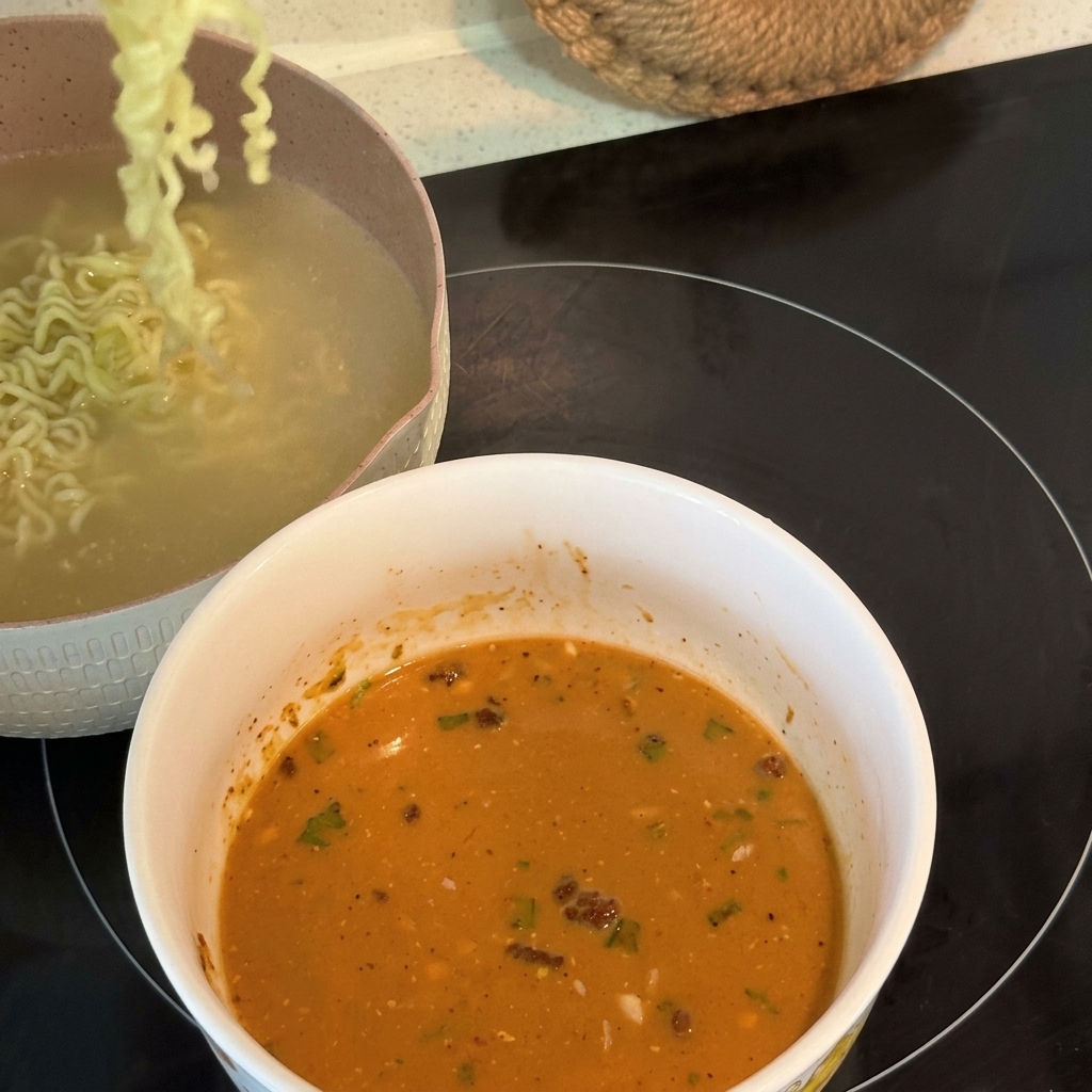 Gekochte lockige Ramen-Nudeln werden angehoben und in eine Schüssel mit cremiger, emulgierter Suppenbasis gegeben.
