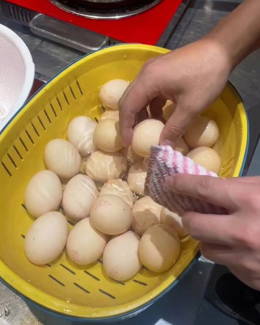 Eier werden in einem gelben Sieb mit einem Schwamm gereinigt.