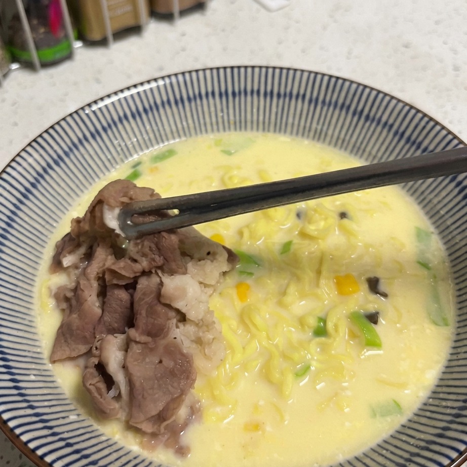 Ein Löffel mit goldenen Maiskörnern wird über eine Schüssel Ramen gestreut.