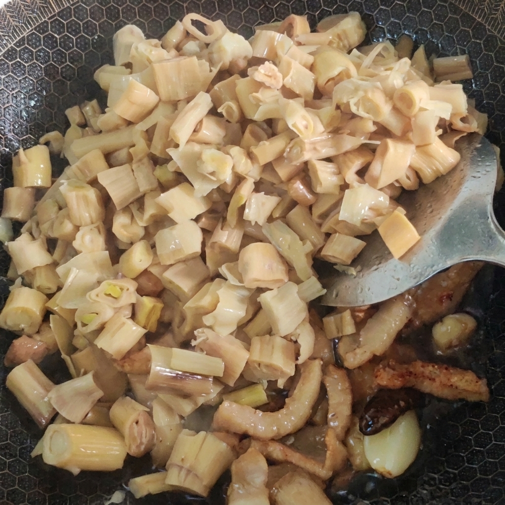 Wasser und eingelegtes Senfgemüse werden in einen Wok mit gebratenem Schweinefleisch und Bambussprossen gegeben.
