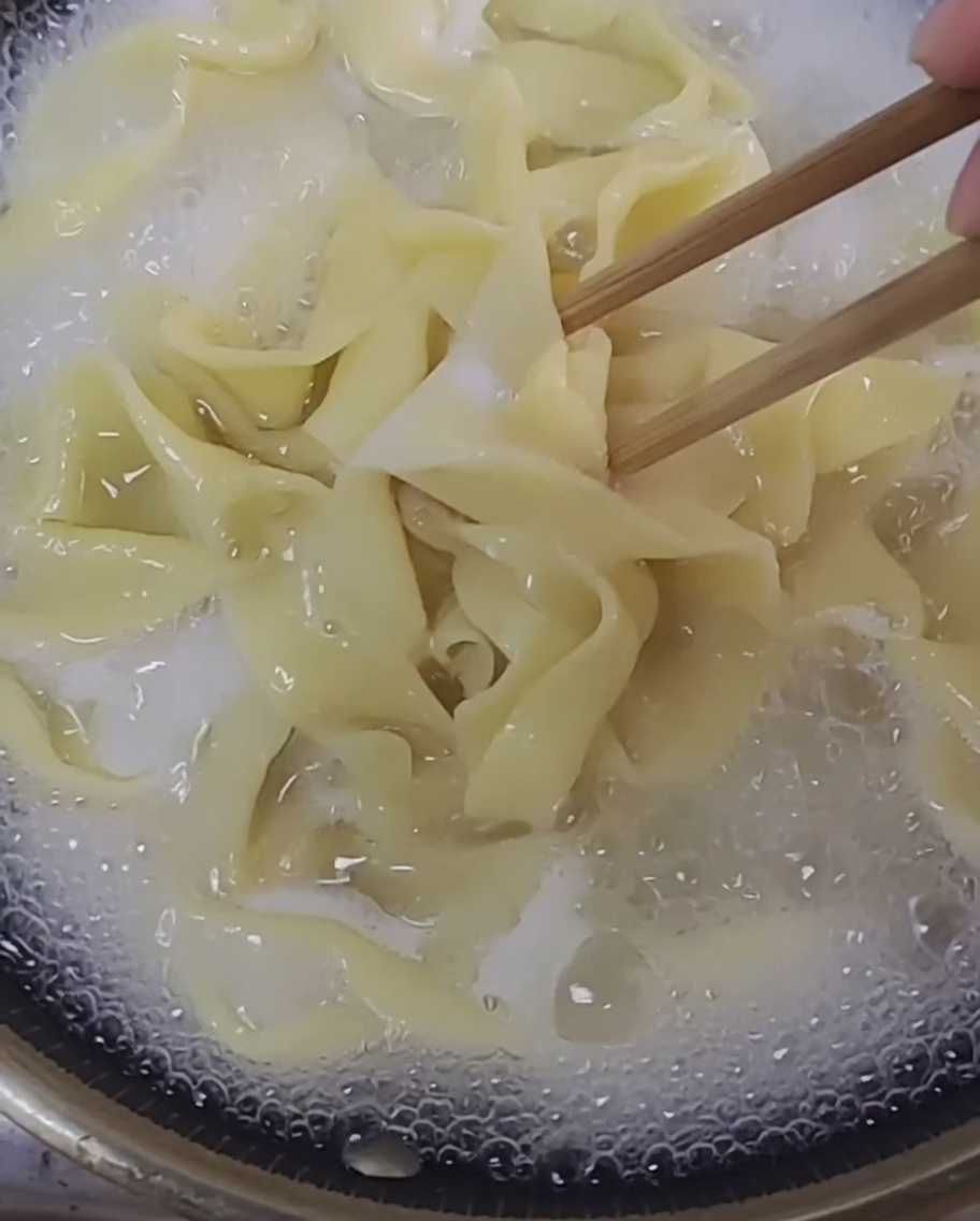 Frisch hergestellte Nudelstränge kochen in einem klaren Topf mit Wasser.