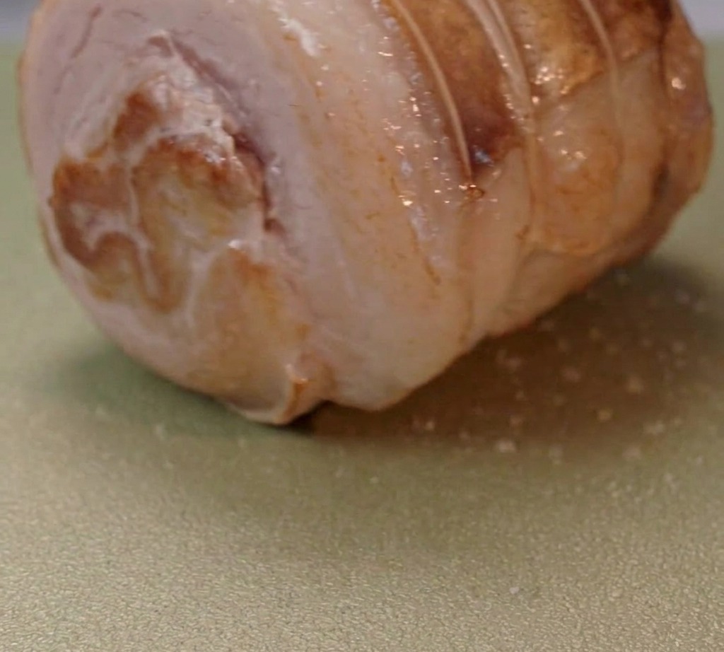 Aufgerollter Schweinebauch bräunt in einer Pfanne mit heißem Öl.