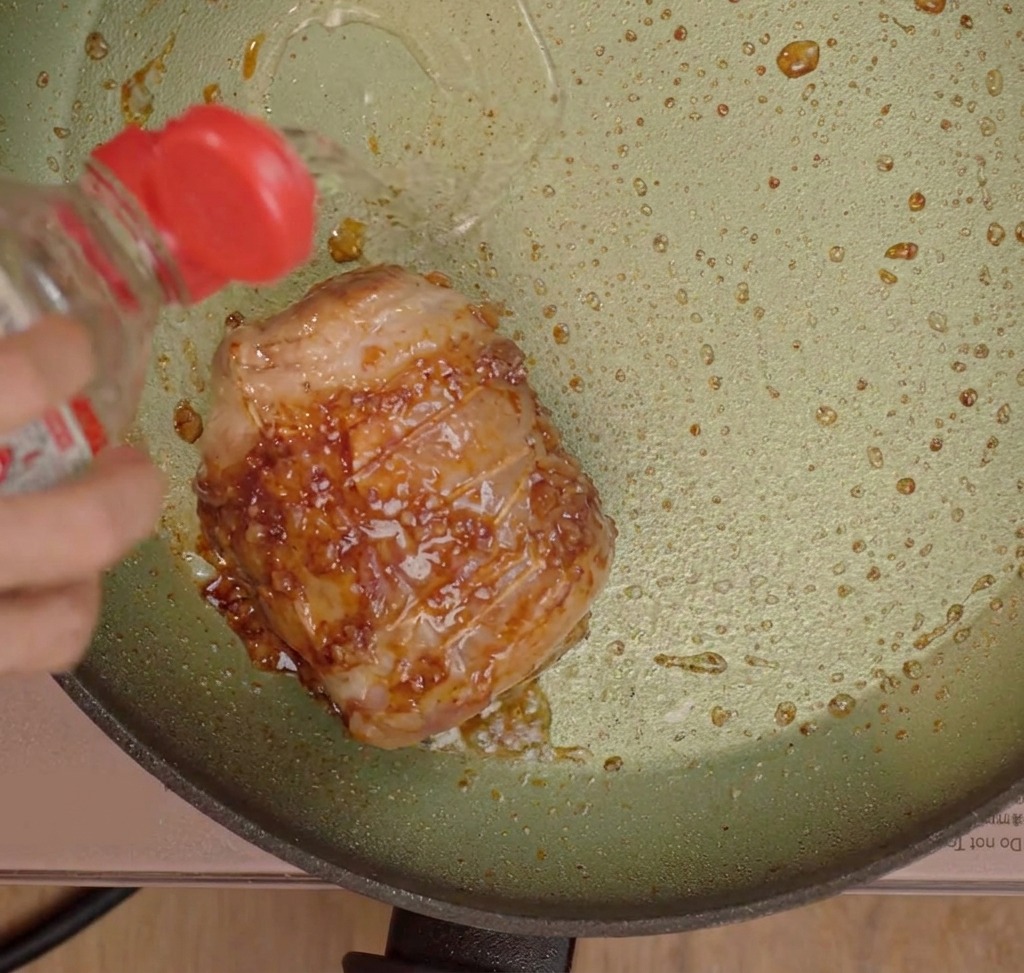 Würzflüssigkeiten werden über den angebratenen Schweinebauch in der Pfanne gegossen.