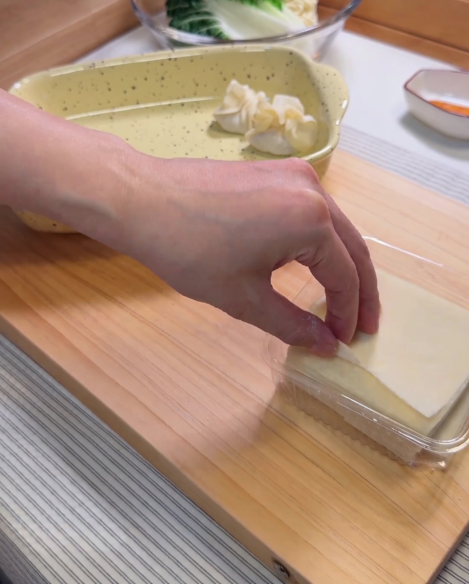 Ein rohes Wan-Tan-Teigblatt auf einer Handfläche, in dessen Mitte eine Portion Garnelenpaste gespritzt wird.