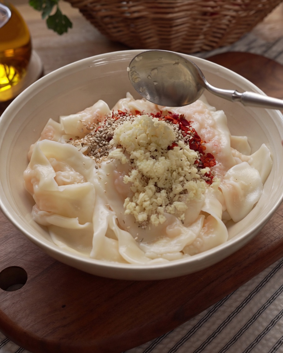 Heißes Öl wird aus einer Kelle über Gewürze und Knoblauch gegossen, die daraufhin zischen.