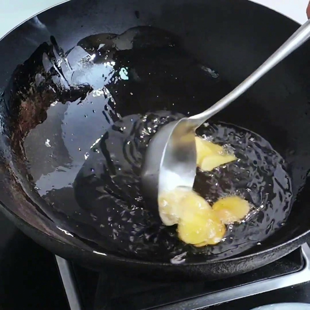 Ingwerscheiben und Garnelenköpfe brutzeln in einer Pfanne mit heißem Öl.