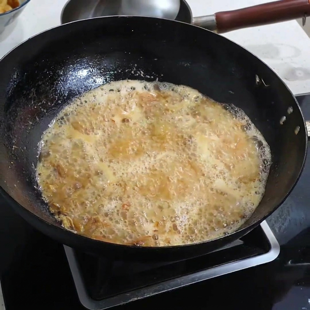 Salz wird in eine sprudelnde, gold-orangefarbene Garnelenbrühe gestreut.