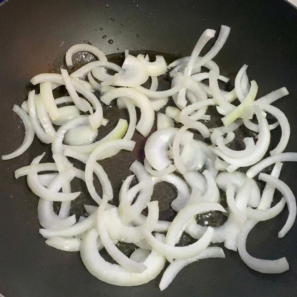 Zwiebelstreifen werden in einer Pfanne mit Öl angedünstet.