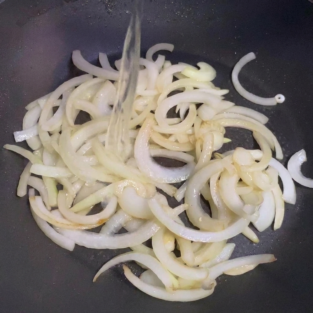 Sake wird in die Pfanne zu den angedünsteten Zwiebeln gegossen.