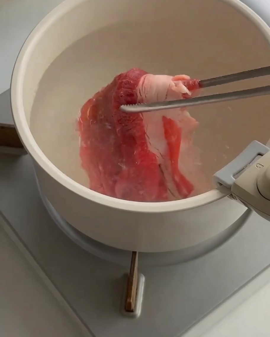 Dünne Rindfleischscheiben werden mit einer Zange in kochendes Wasser gegeben.