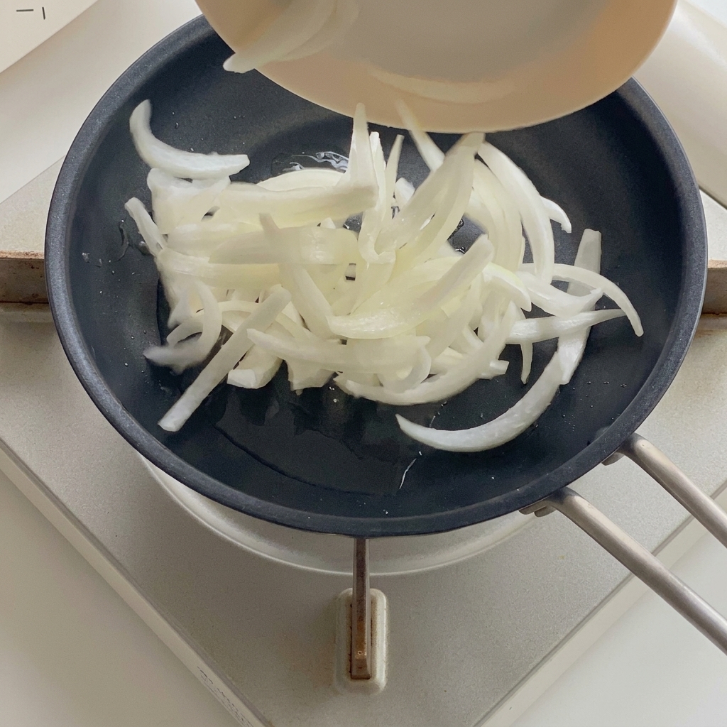 Zwiebeln in einer Pfanne mit Öl werden glasig gedünstet.