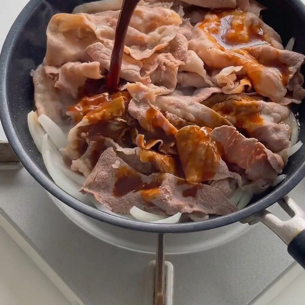 Dunkle Soße wird über Fleisch und Zwiebeln gegossen.