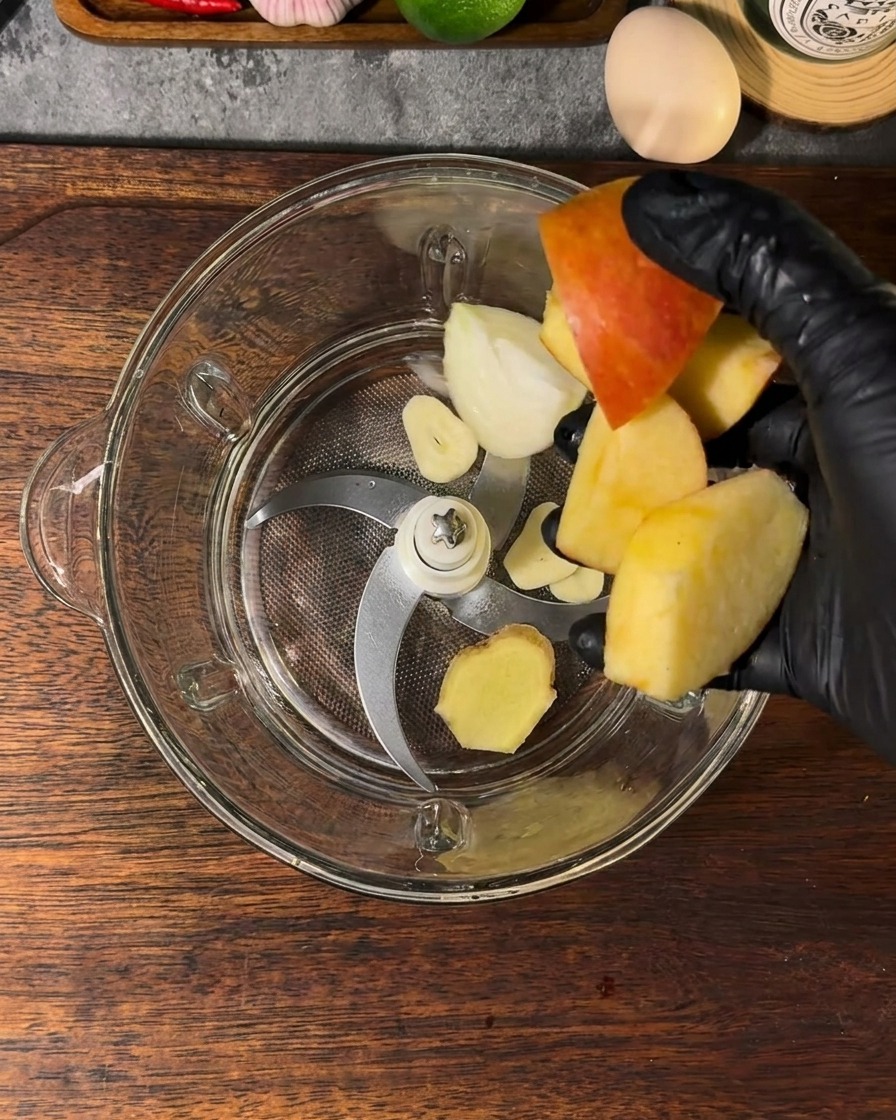 Ein Mixerbehälter gefüllt mit Apfelstücken, Zwiebeln, Knoblauch, Ingwer und Wasser.