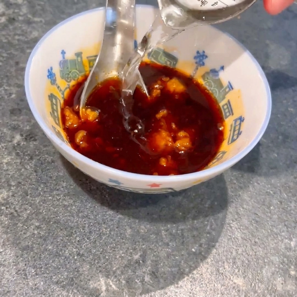 Wasser wird in eine kleine Schüssel mit dunkler Sojasauce und Miso-Stücken gegossen, während ein Löffel die Mischung umrührt.
