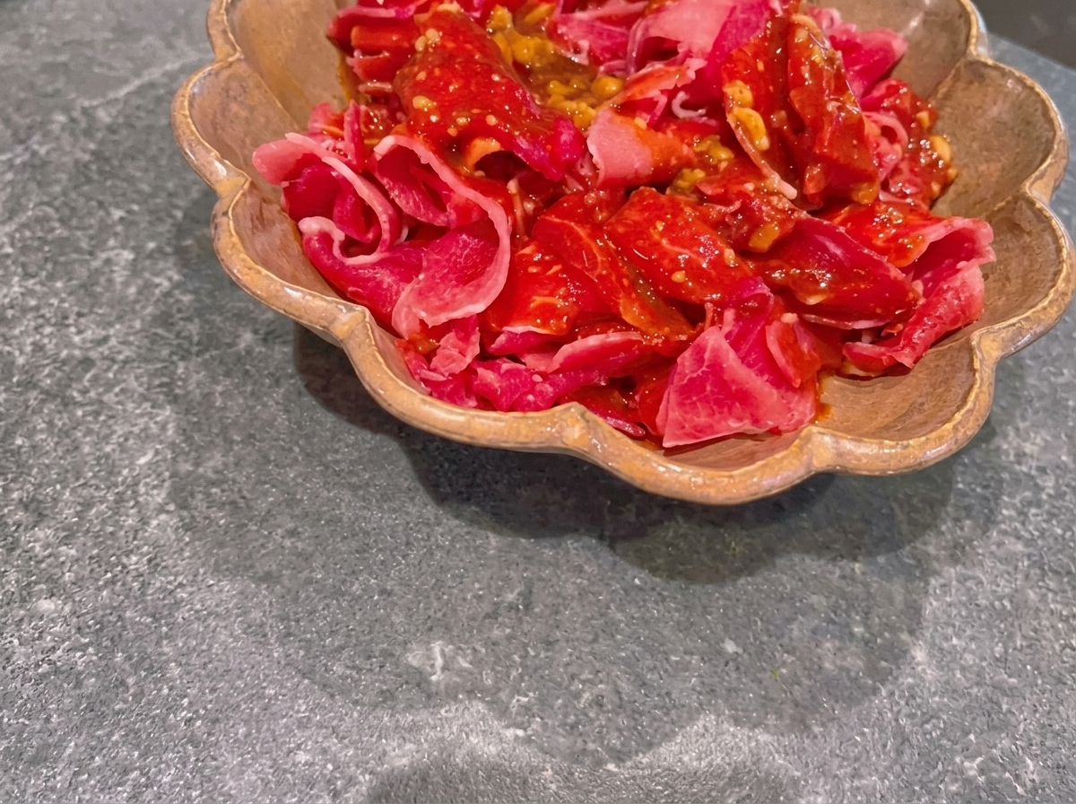 Dünn geschnittenes rohes Rindfleisch, das in einer braunen, gewellten Form mit einer dunklen Miso-Marinade überzogen ist.