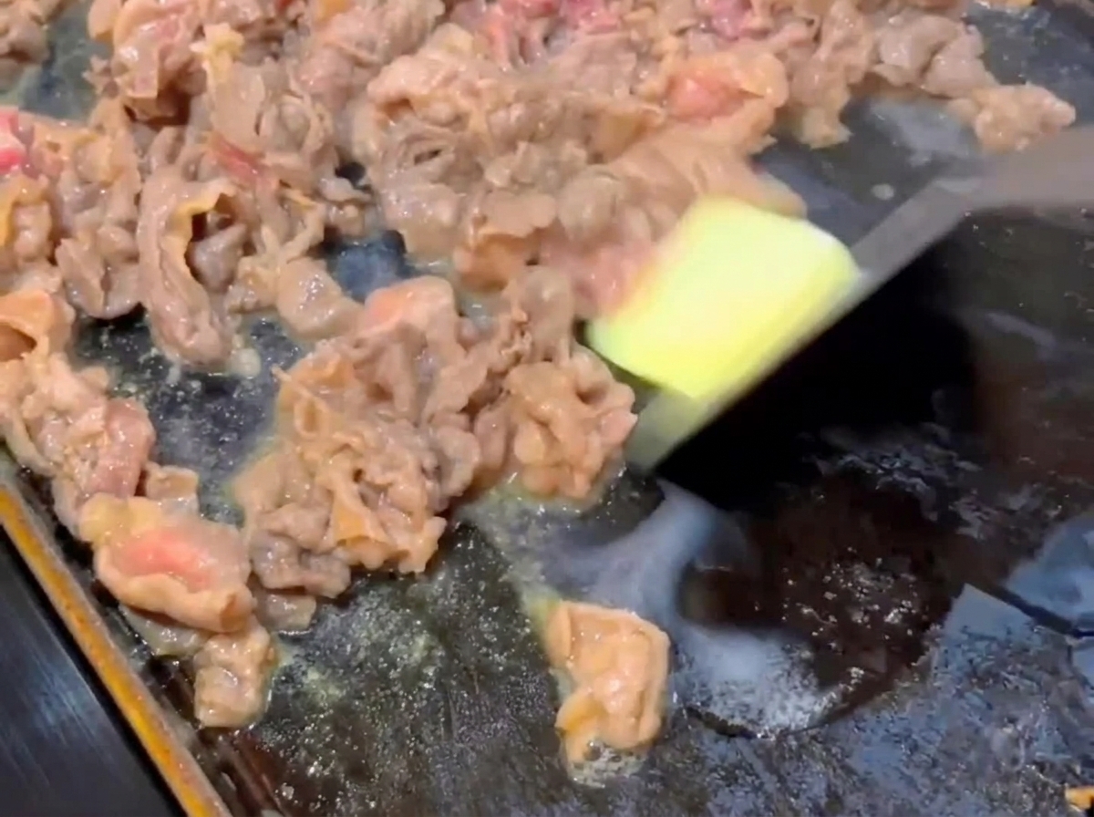 Ein kleines quadratisches Stück Butter schmilzt auf teilweise gebratenen Rindfleischscheiben in einer heißen flachen Pfanne.
