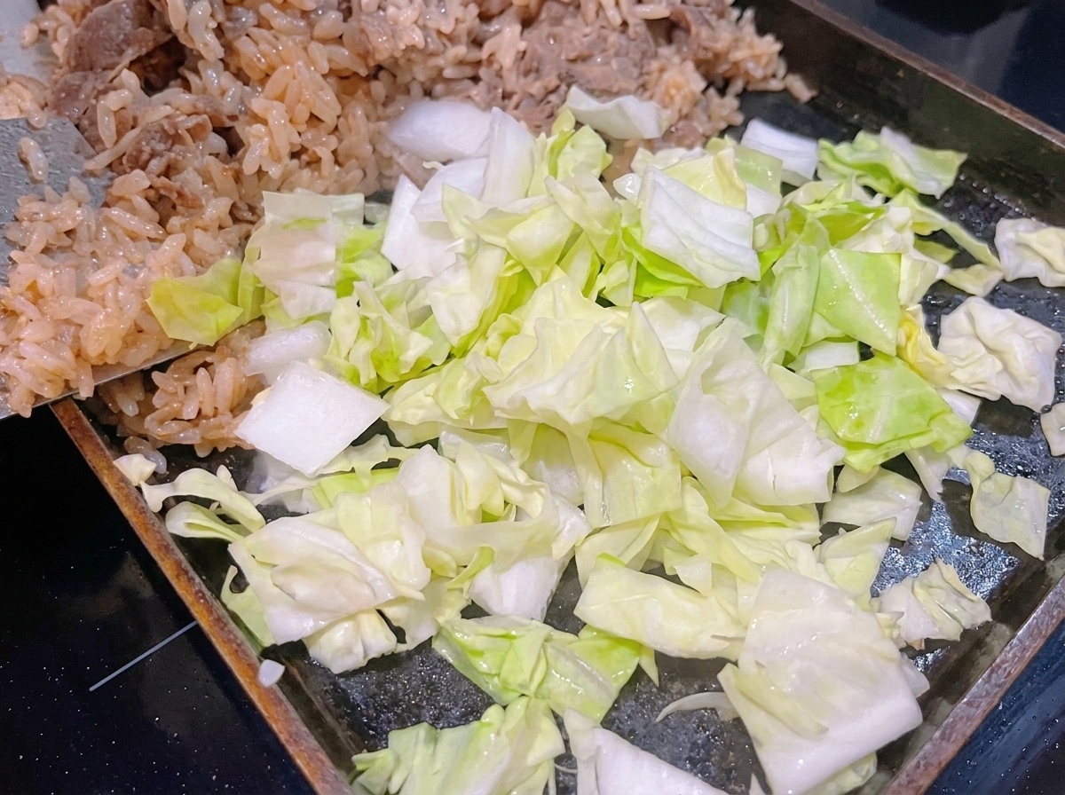 Frisch gehackter grüner Kohl liegt auf weißem Reis und Rindfleisch in einer heißen Pfanne.
