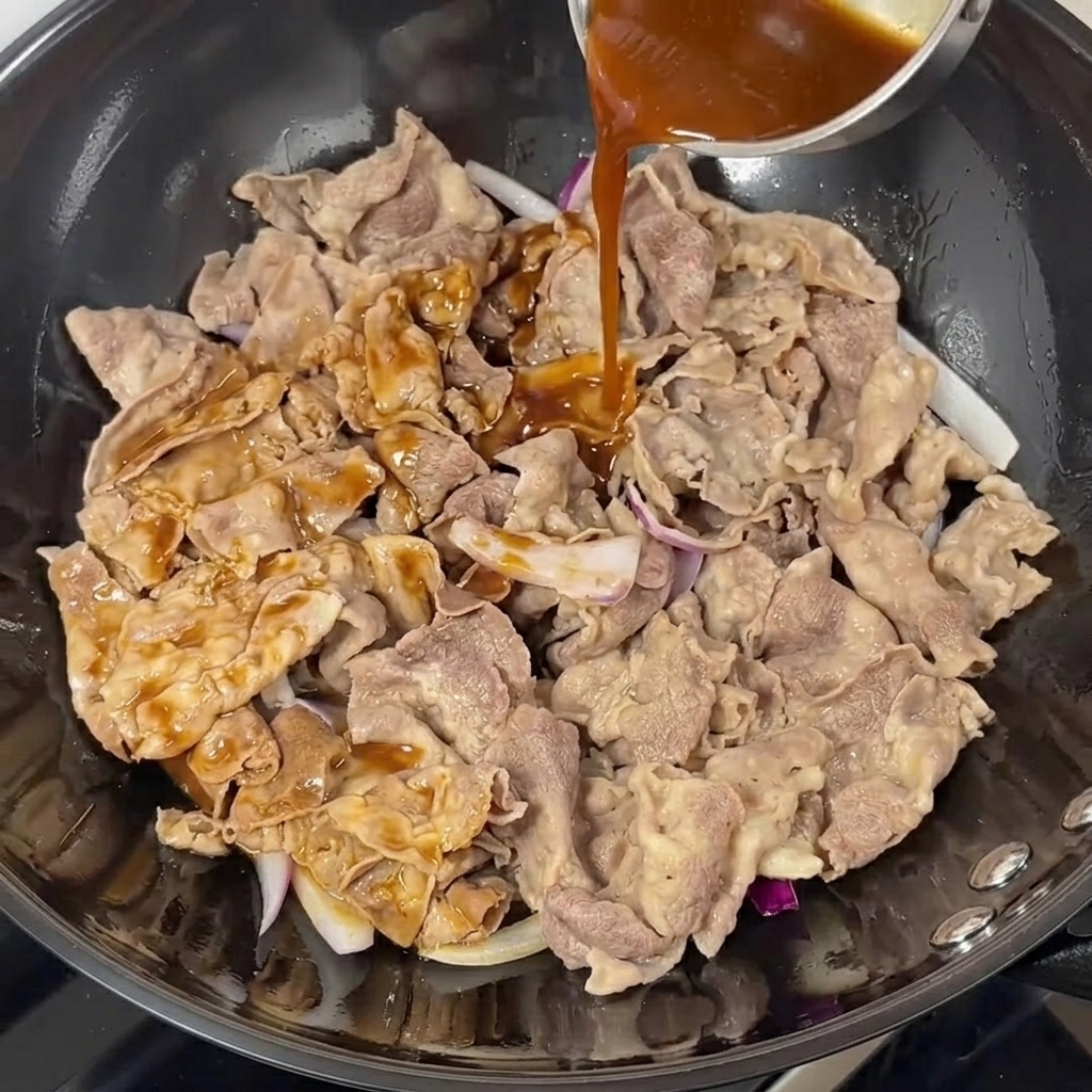 Dunkle Teriyaki-Sauce wird über das Rindfleisch und die Zwiebeln im Wok gegossen.