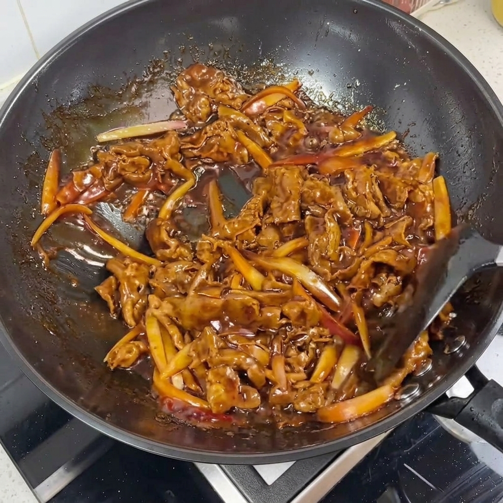 Nahaufnahme von Rindfleisch und Zwiebelstreifen, die mit einer glänzenden Teriyaki-Sauce überzogen werden.