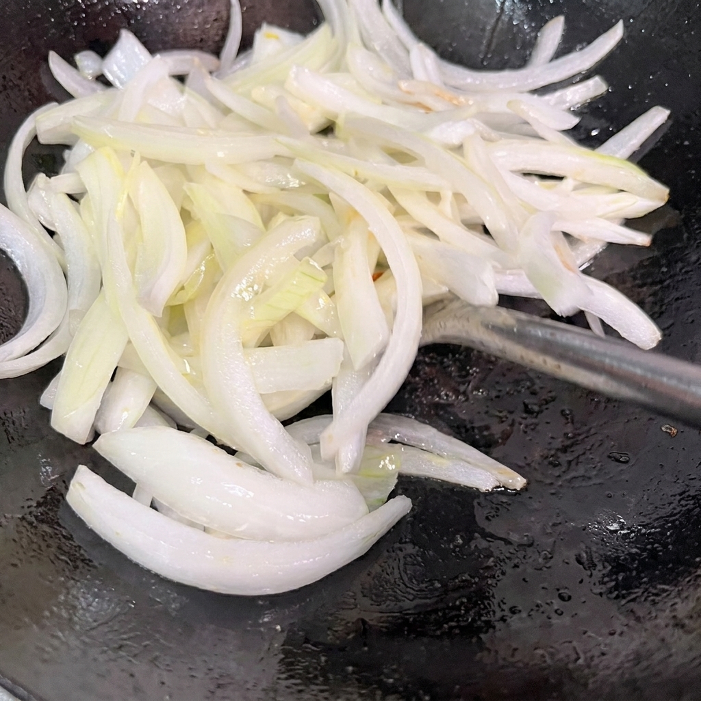 In Scheiben geschnittene Zwiebeln werden in einem heißen Wok angebraten.