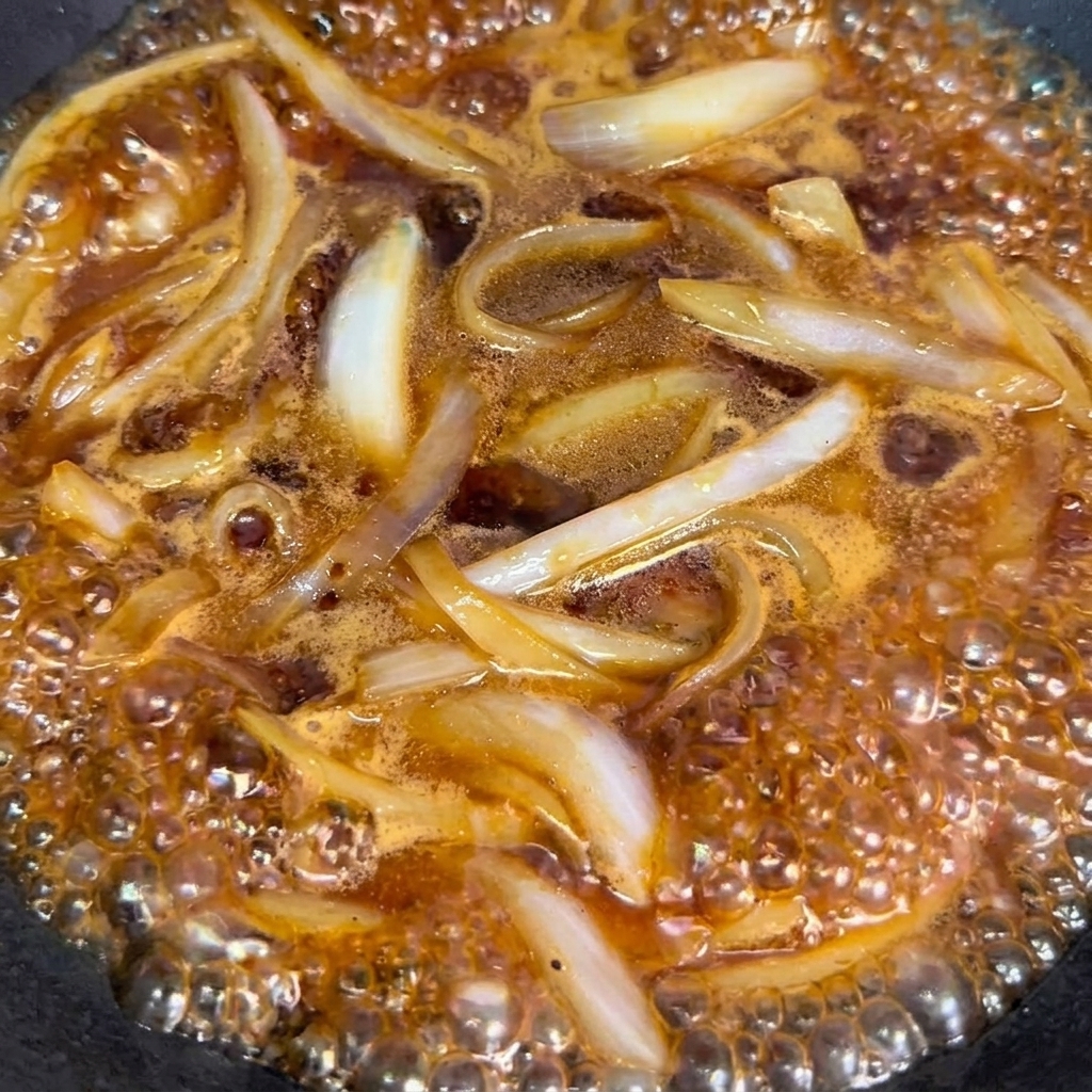 Das blanchierte Rindfleisch wird zu Zwiebeln und Sauce in den Wok gegeben.