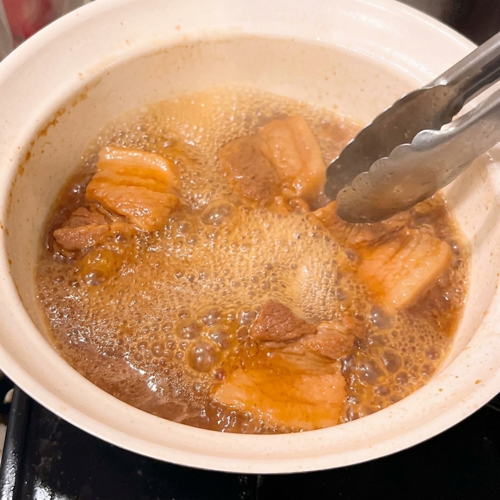 Nahaufnahme von zarten Schweinefleischstücken, die in einer eingedickten, blubbernden Miso-Glasur schmoren.