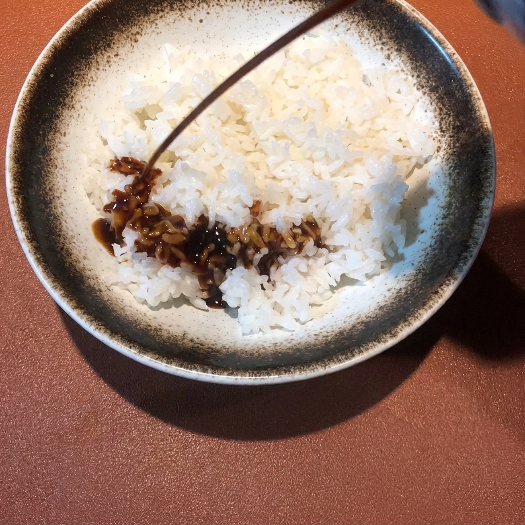 Dunkle Sauce wird über eine Schüssel mit dampfendem Reis geträufelt.