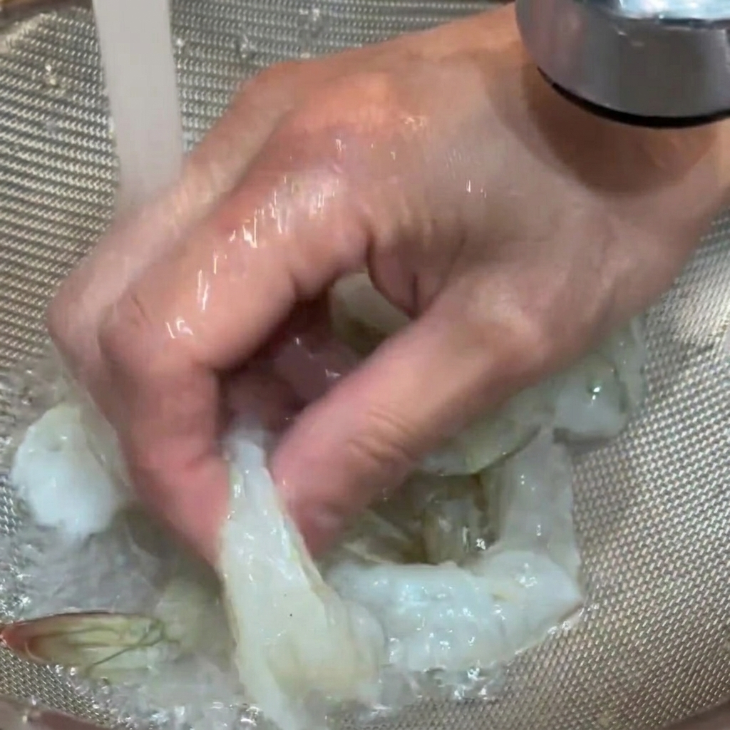 Rohe Garnelen werden in einem Sieb unter fließendem Wasser abgespült.