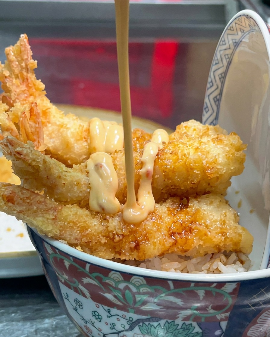 Cremige hellorangefarbene Sauce wird in Linien über die frittierten Garnelen geträufelt.