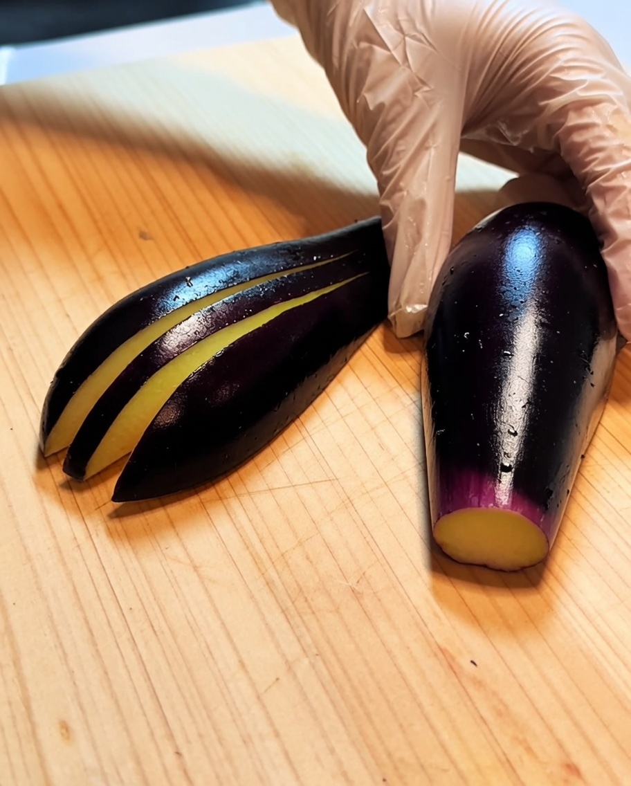 Eine Aubergine auf einem Holzbrett mit mehreren parallelen, flachen Schnitten entlang der Länge.