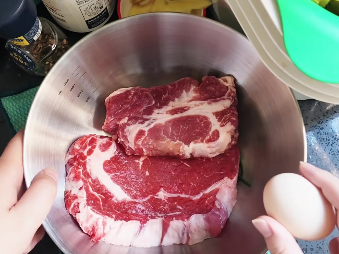 Ein rohes Ei wird über frische Schweinekoteletts in einer Edelstahlschüssel aufgeschlagen.