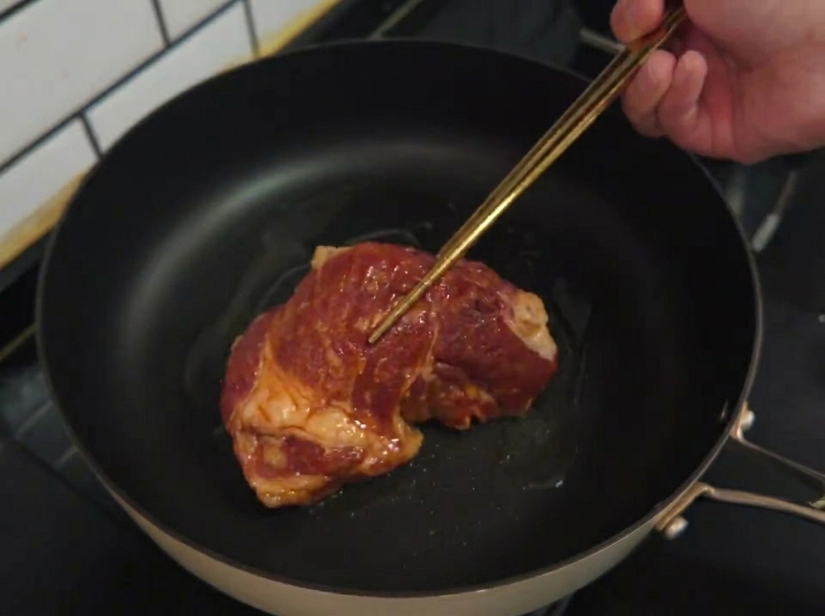 Ein rohes mariniertes Schweinekotelett wird in eine heiße Pfanne mit Speiseöl gelegt.