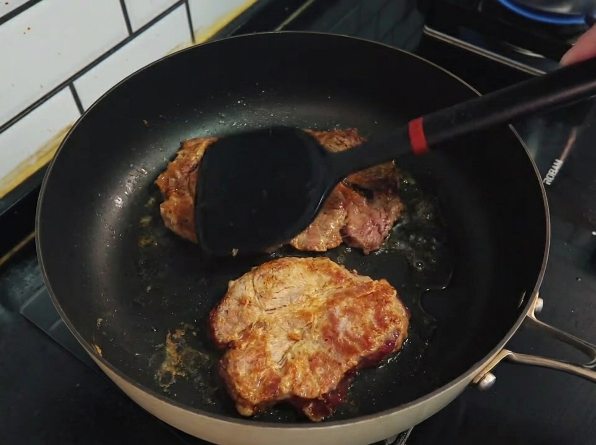 Ein Pfannenwender wendet gebräunte Schweinekoteletts in einer Antihaftpfanne.