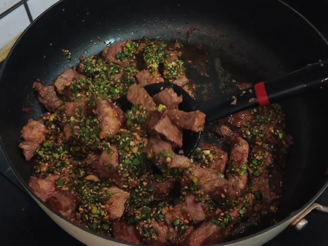 Ein schwarzer Pfannenwender mischt Kotelettstreifen mit einer grünen Frühlingszwiebel-Sauce in einer Pfanne.