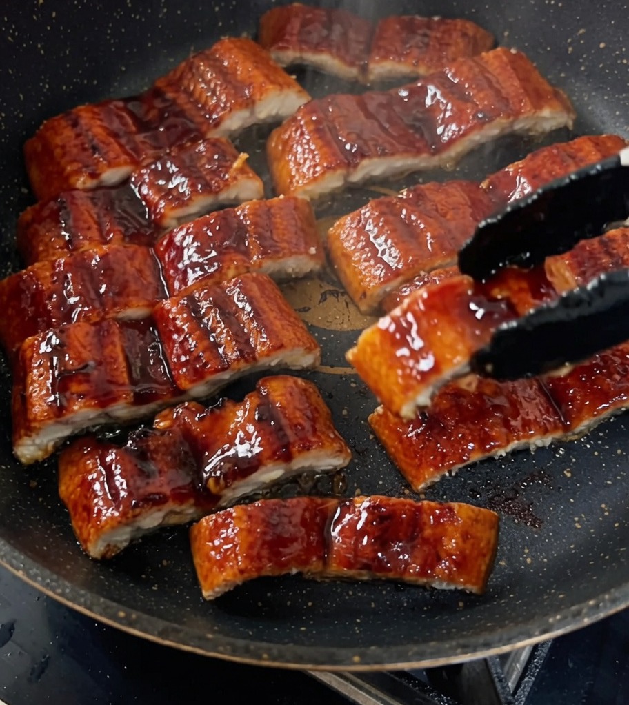 Gegrillte Aalstücke werden in einer Pfanne mit einer dunklen, reichhaltigen Sauce glasiert.