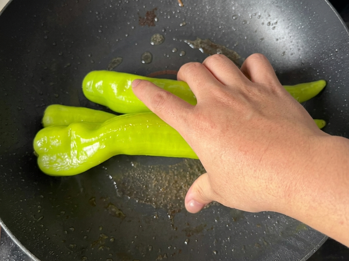 Grüne Paprika braten in der Pfanne, bis die Haut Blasen wirft.