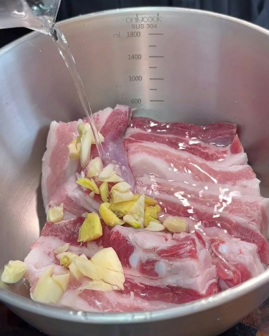 Eine Schüssel mit Schweinebauchstreifen, die mit gehackten Gewürzen und roter fermentierter Tofupaste gewürzt werden.