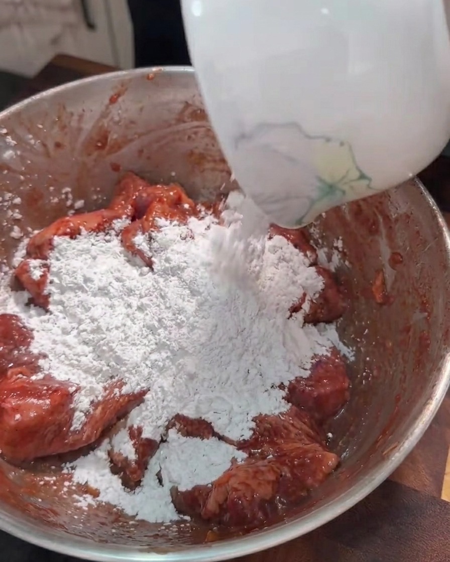 Süßkartoffelstärke wird in eine Schüssel mit marinierten Schweinebauchstreifen gegeben.