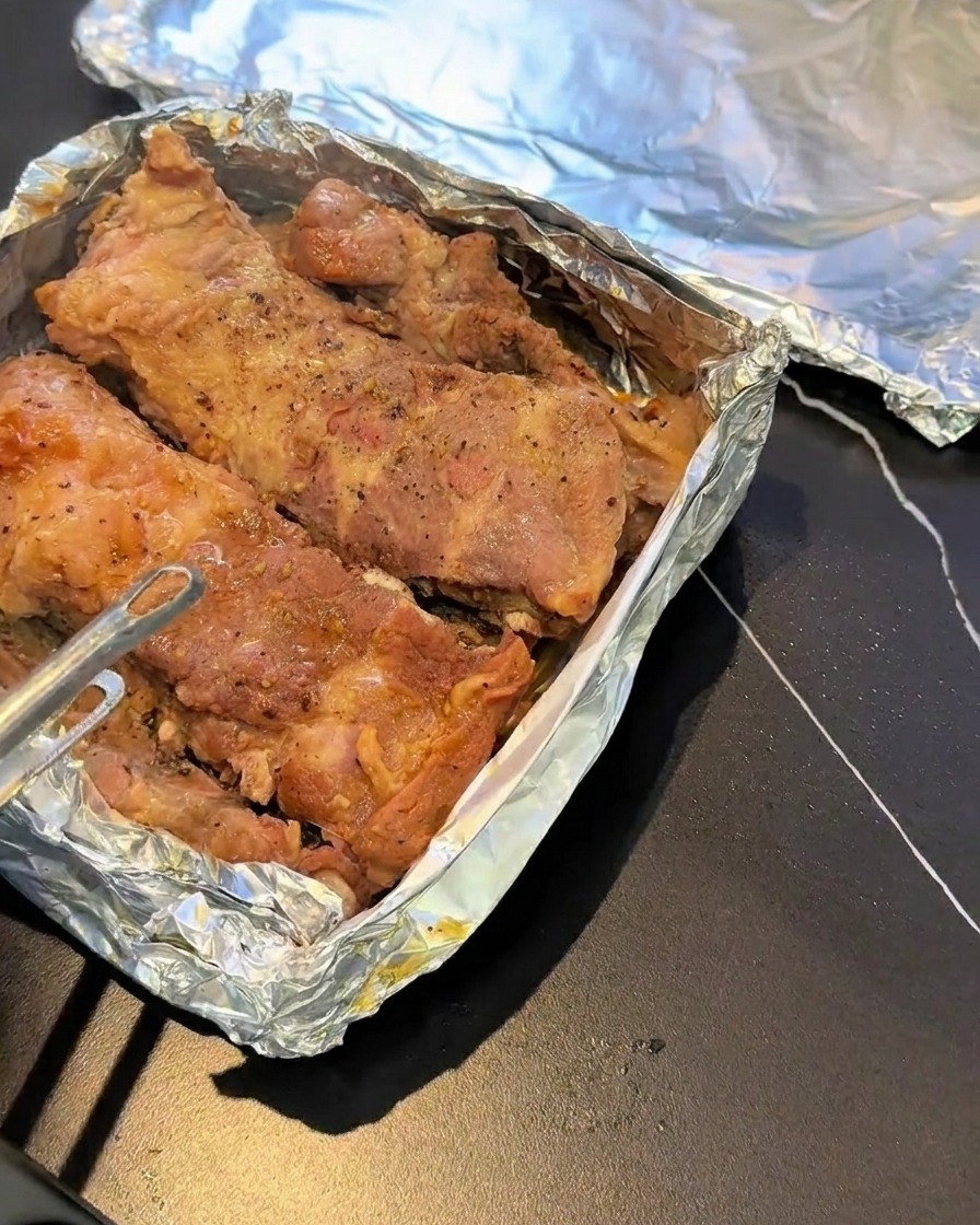 Gedämpfte Schweinerippchen ruhen auf einem mit Folie ausgekleideten Backblech, gewürzt mit schwarzem Pfeffer.