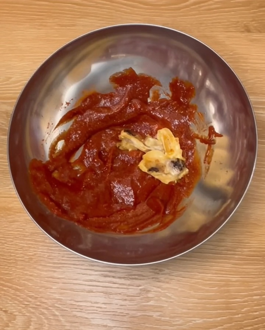 Gebackene Hähnchenkeulen werden in einer Edelstahlschüssel mit roter koreanischer Sauce vermengt.