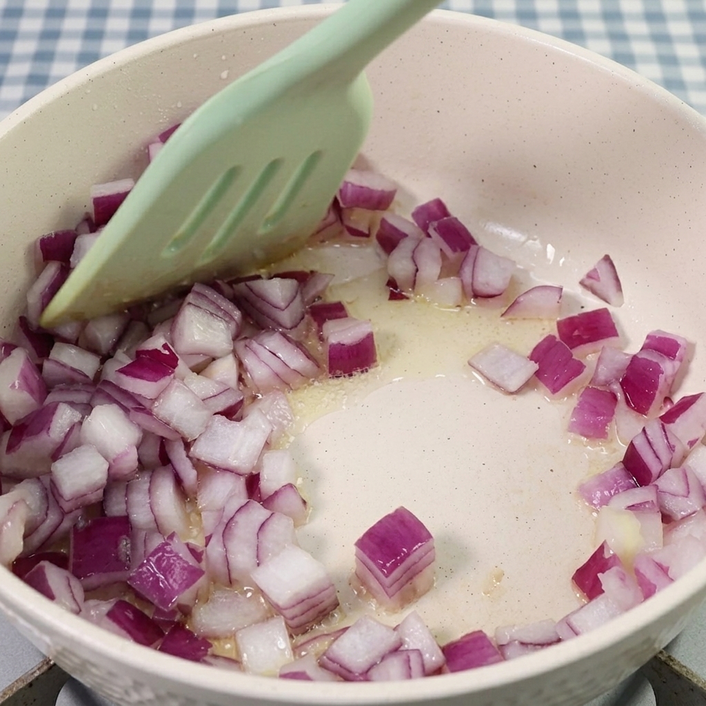 Gewürfelte rote Zwiebeln werden in einem Topf mit einem Silikonspatel angebraten.