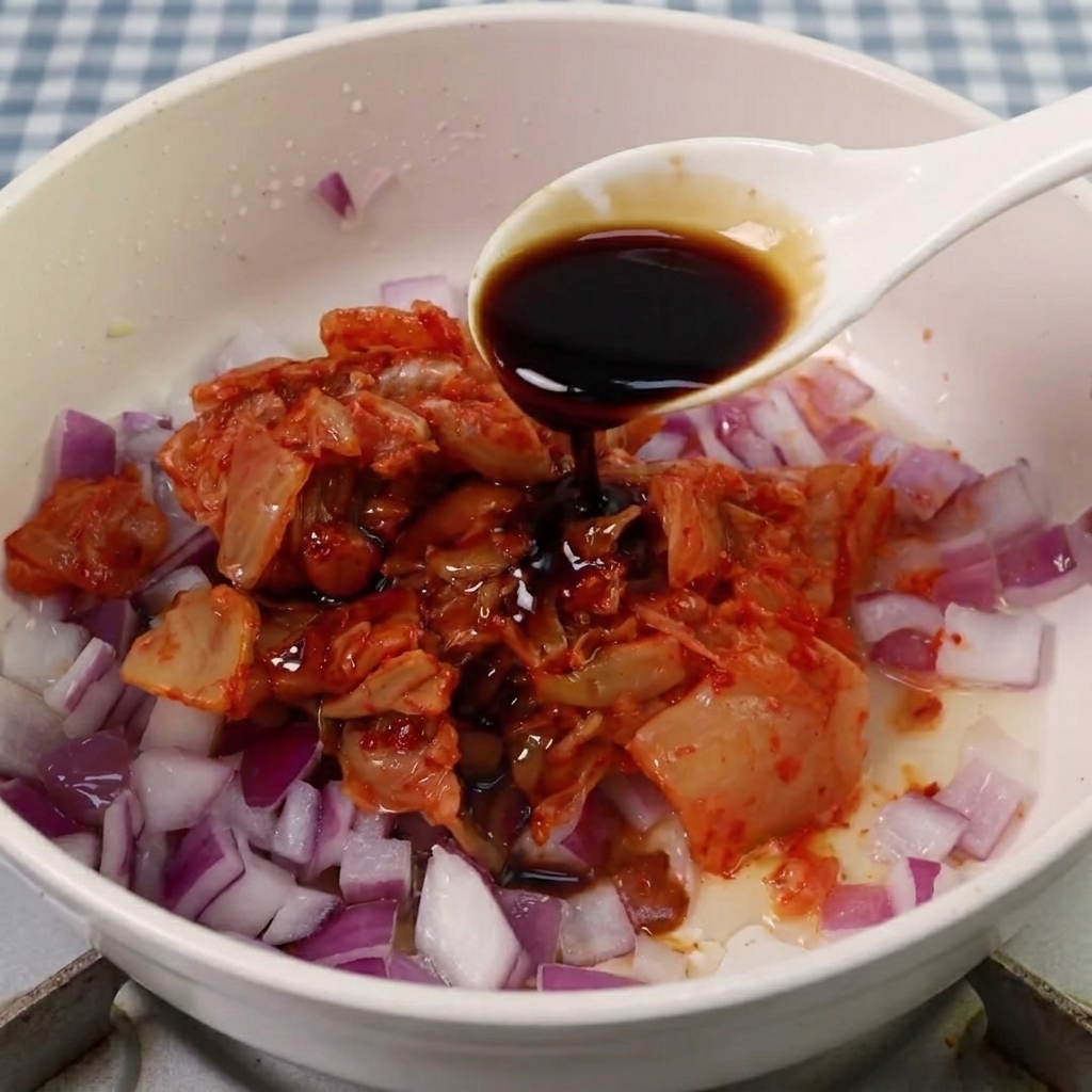 Sojasauce, Zucker und koreanische Würzpaste werden zur Kimchi-Zwiebel-Mischung gegeben.