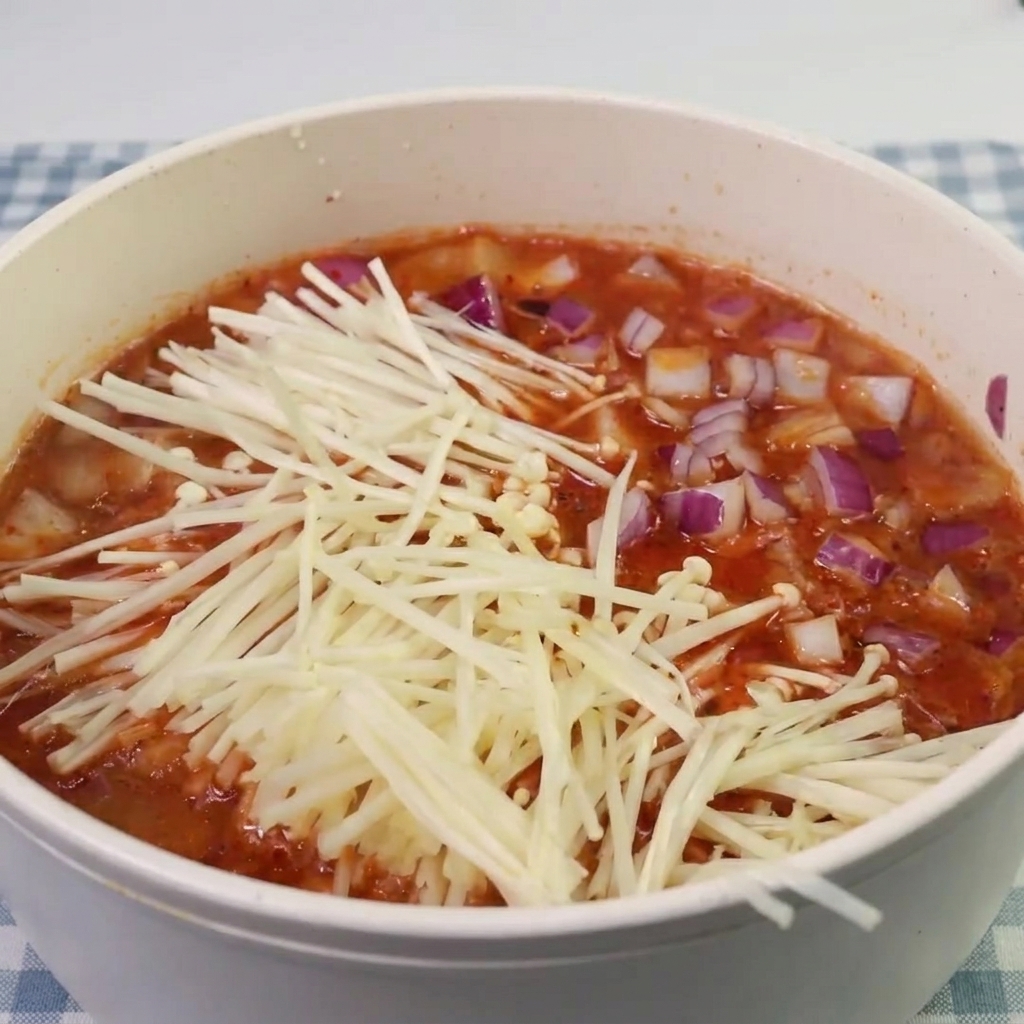Enoki-Pilze und Spam-Stücke werden in die köchelnde Kimchi-Suppe gegeben.